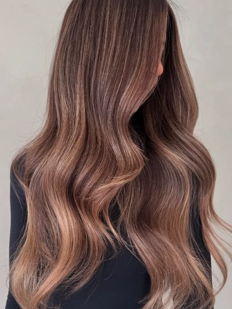 Capelli lunghi castani con riflessi rosati e onde morbide, su fondo chiaro