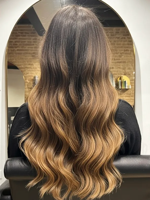Capelli lunghi con sfumatura dal castano al miele, visti da dietro davanti allo specchio ad arco del salone